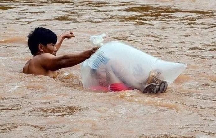 Pai coloca saco plástico em filho para que não se molhe no rio ao fazer travessia para escola
